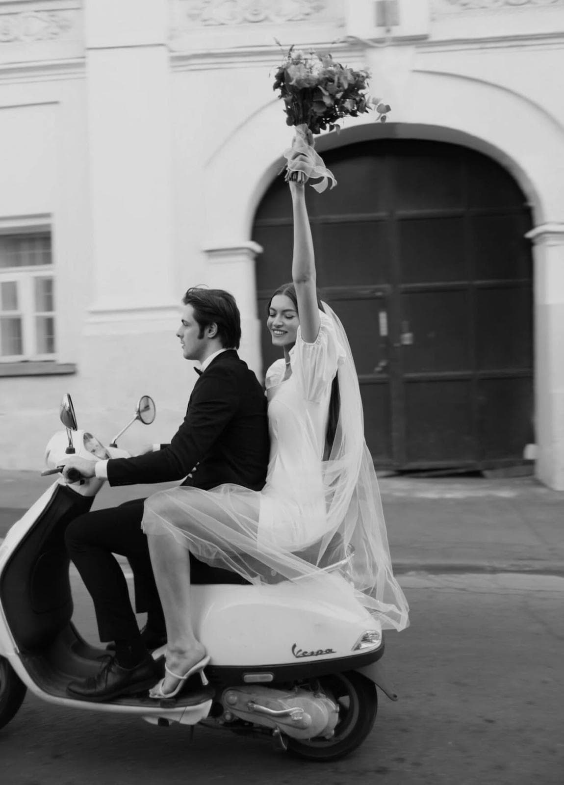 Novios recién casados en Vespa, ella con el ramo en alto